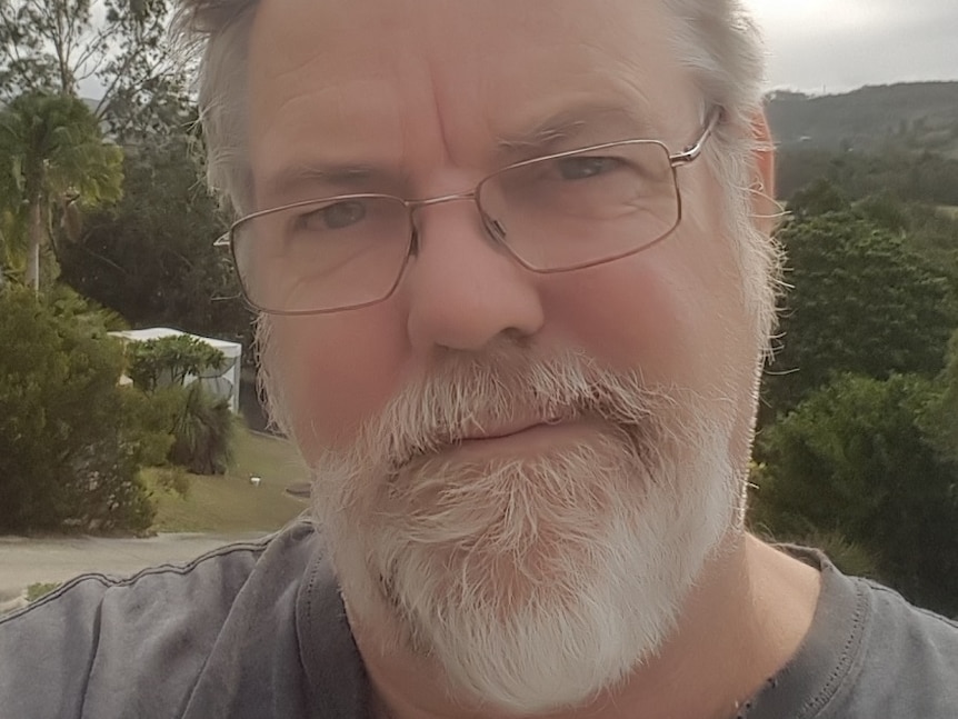 A selfie taken outside of a man with a white beard, short grey hair and glasses.