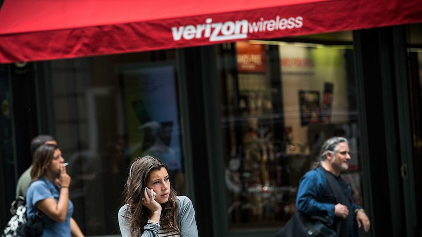 A woman uses her phone while walking past a Verizon Store in New York City.