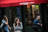 A woman uses her phone while walking past a Verizon Store in New York City.