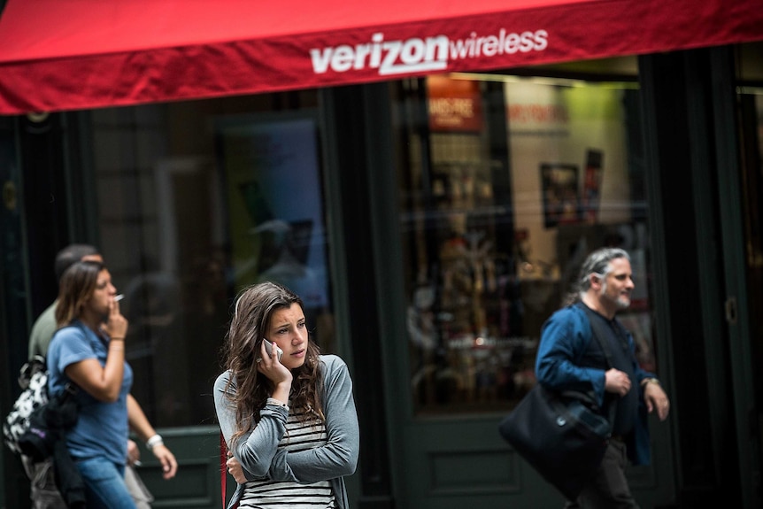 A woman uses her phone while walking past a Verizon Store in New York City.
