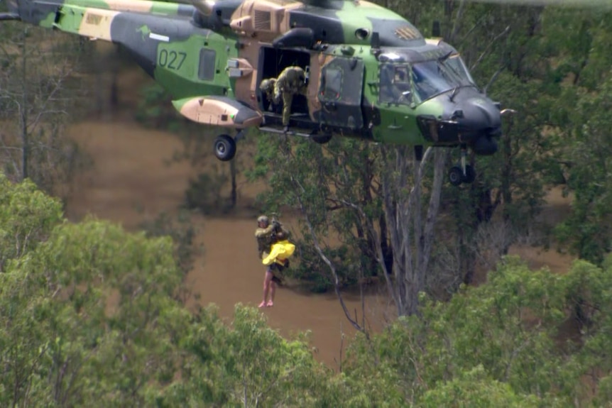 Two people dangling from a helicopter above a large body of water.