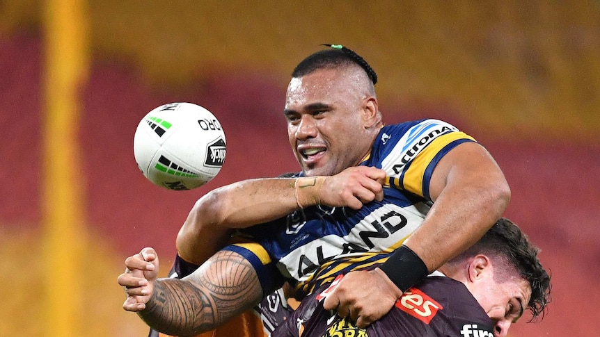 A man is tackled and throws the ball away on a rugby league field