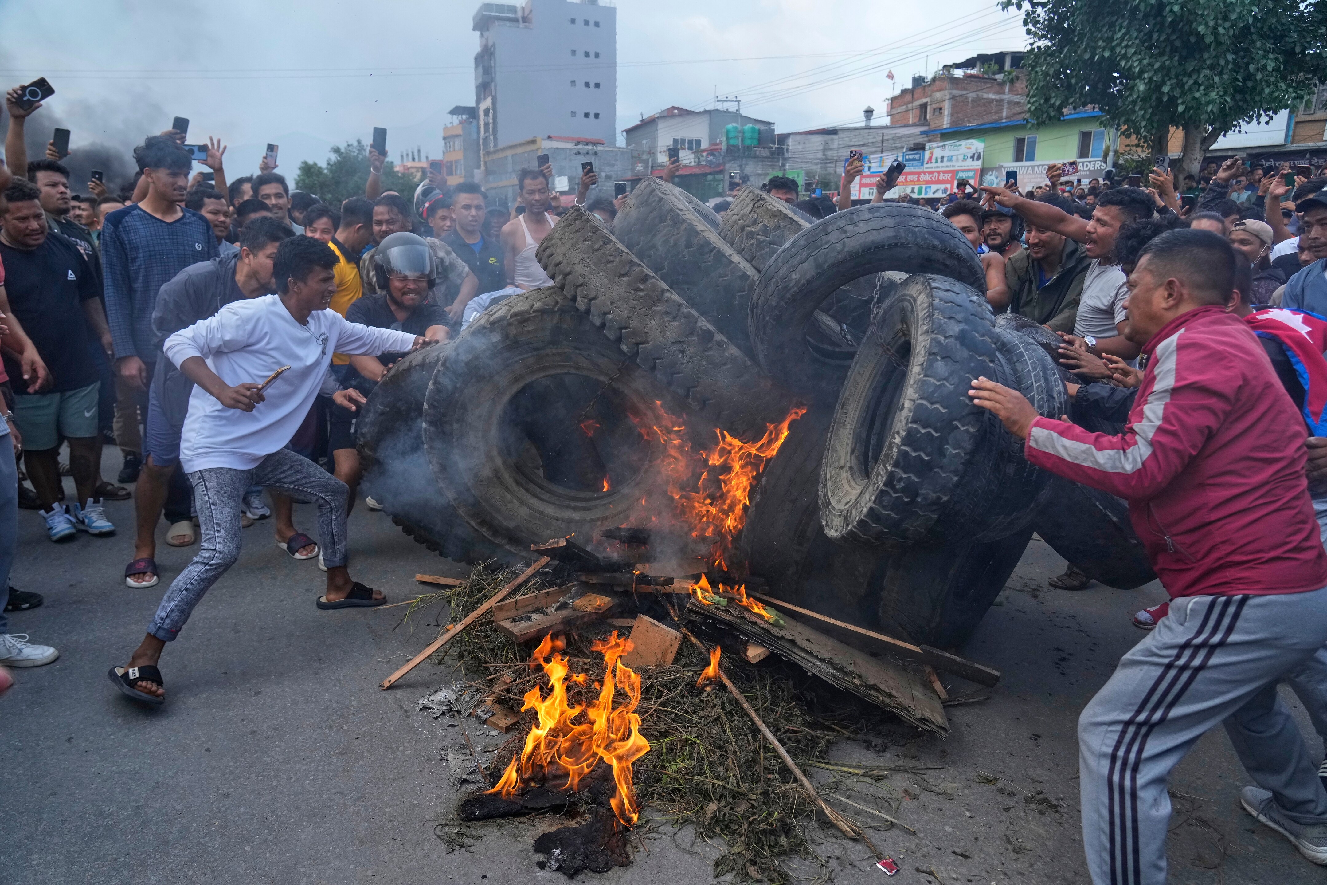 Male Nepalese protesters surrounding a large pile of black truck tyres and orange flames