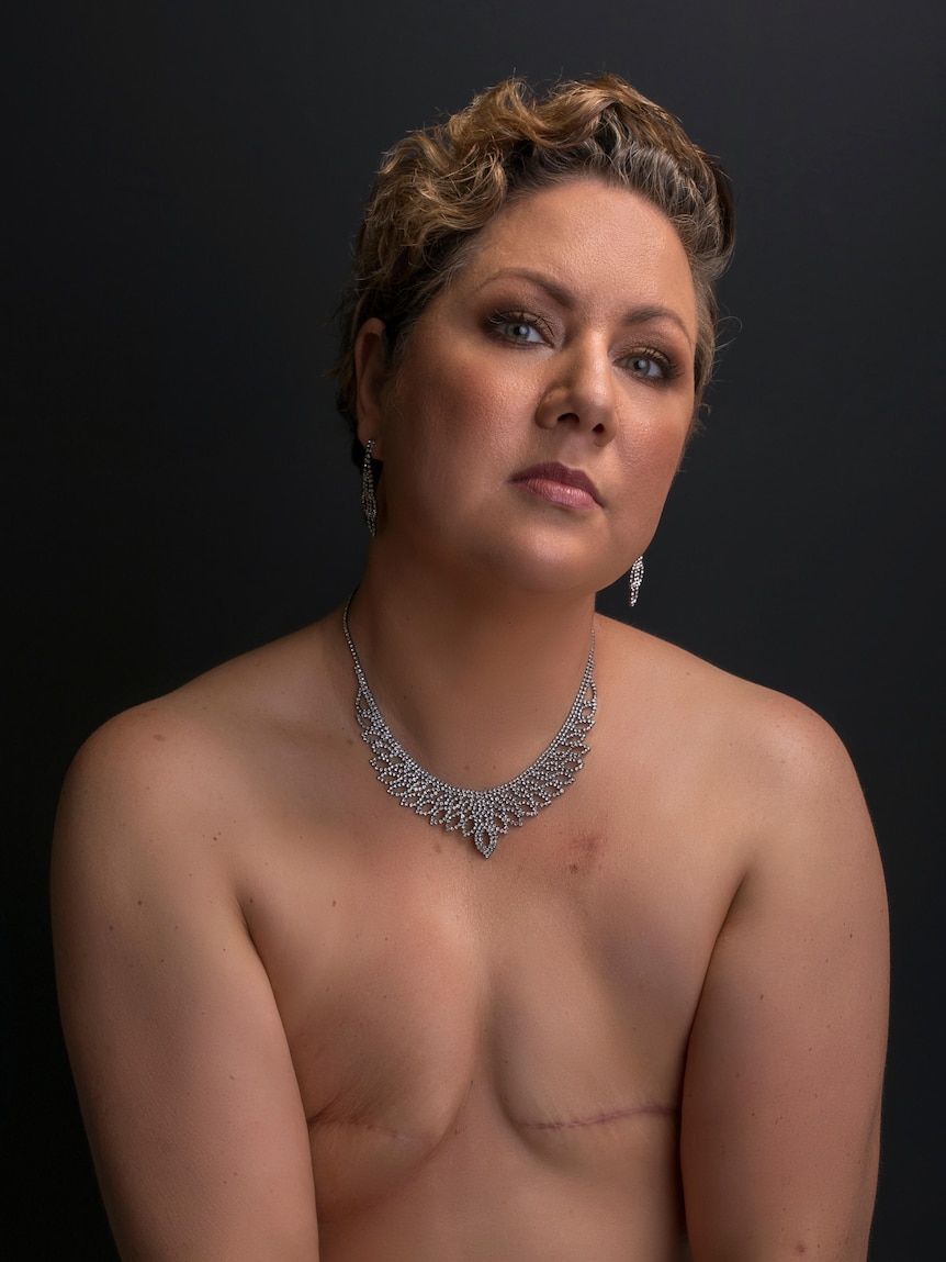 Topless woman with short hair and makeup in a studio portrait with scars on chest where she had breasts removed