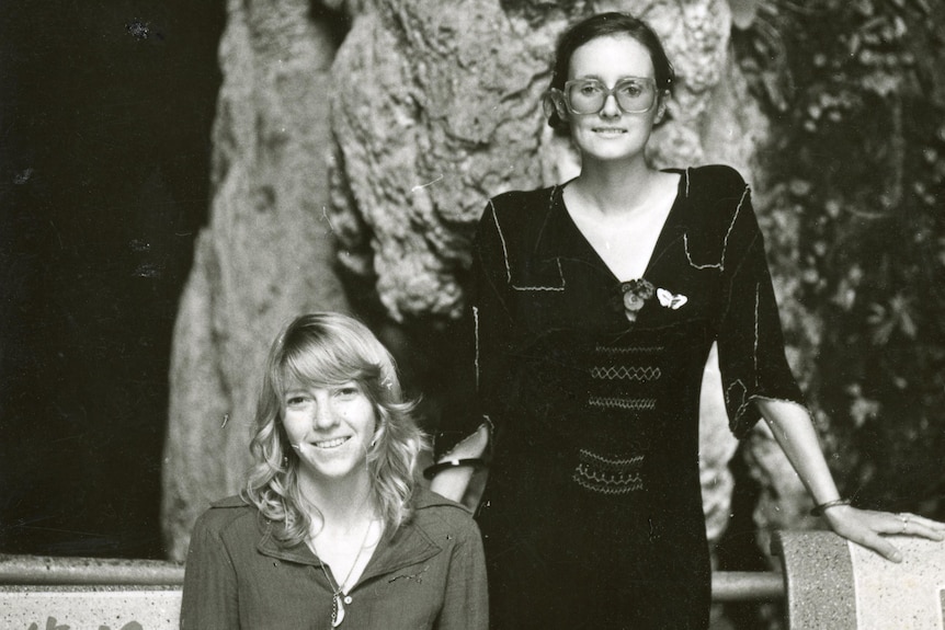 Black and white photo of one woman sitting and another standing next to her.