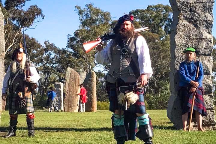 Men in kilts with replica weapons pose in the standing stone circle