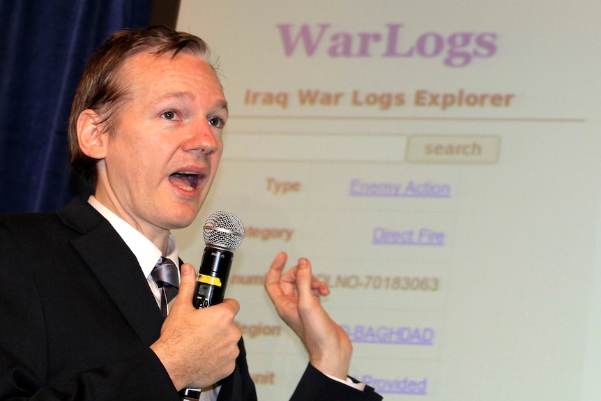 A young man holding a microphone and pointing to a screen with words reading War logs on it