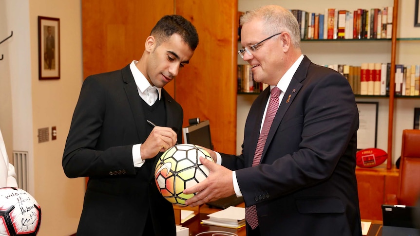 A man signs a football being held by the Prime Minister at Parliament House in Canberra.
