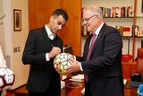 A man signs a football being held by the Prime Minister at Parliament House in Canberra.