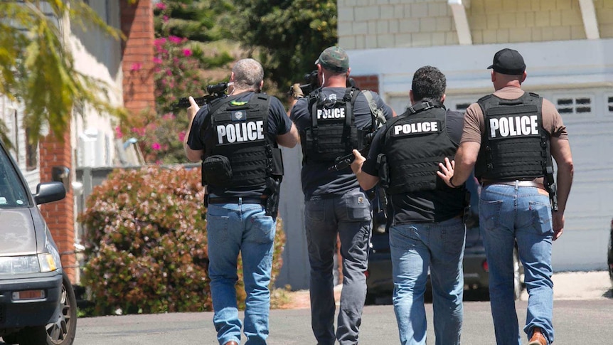 Heavily armed San Diego police officers in light blue jeans approach a suburban home.