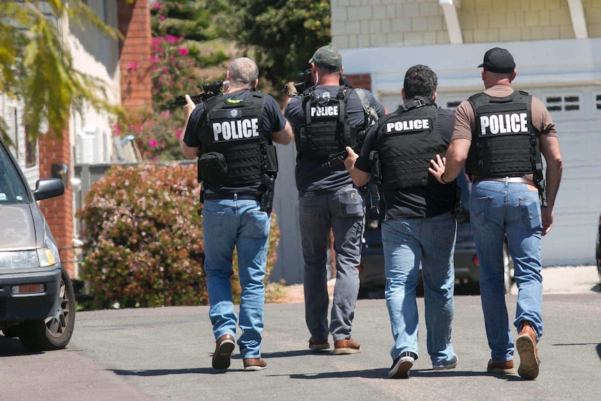 Heavily armed San Diego police officers in light blue jeans approach a suburban home.