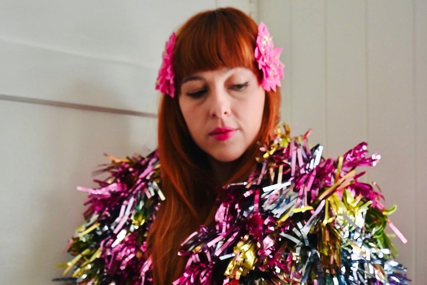 An image of rachel burke, who has red hair, looking down wearing mutli-coloured jacket made of tinsel
