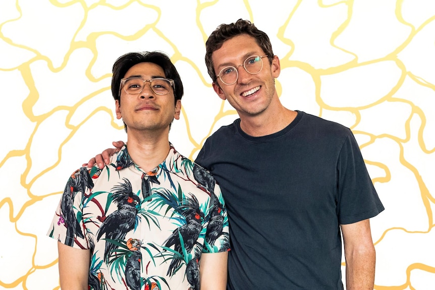 Michael Hing and Lewis Hobba standing in front of a yellow and white mural smiling at the camera