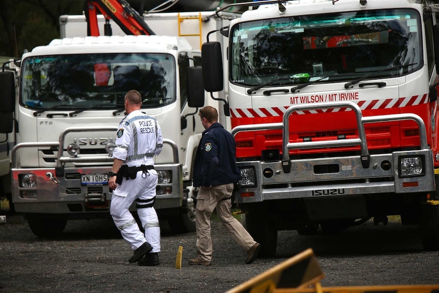 police officers walking pass firetrucks in a rural area