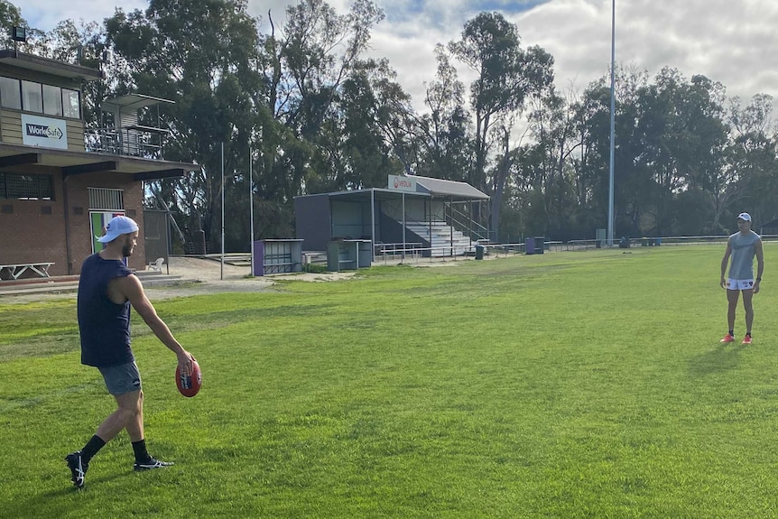 A AFL player is kicking a football to another player