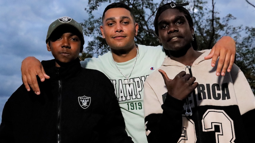 Three young Indigenous men looking at the camera and smiling, wearing hoodies