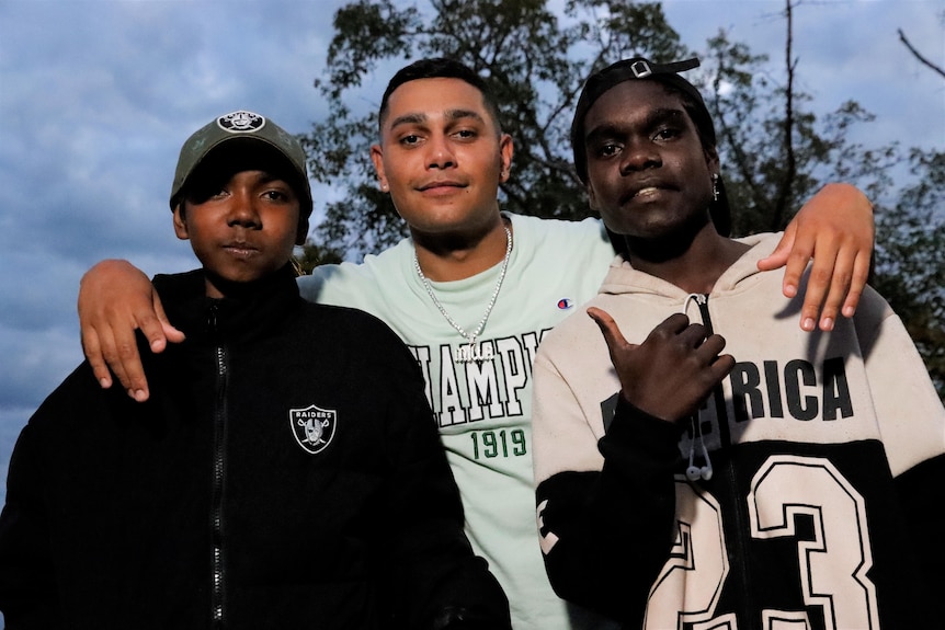 Three young Indigenous men looking at the camera and smiling, wearing hoodies