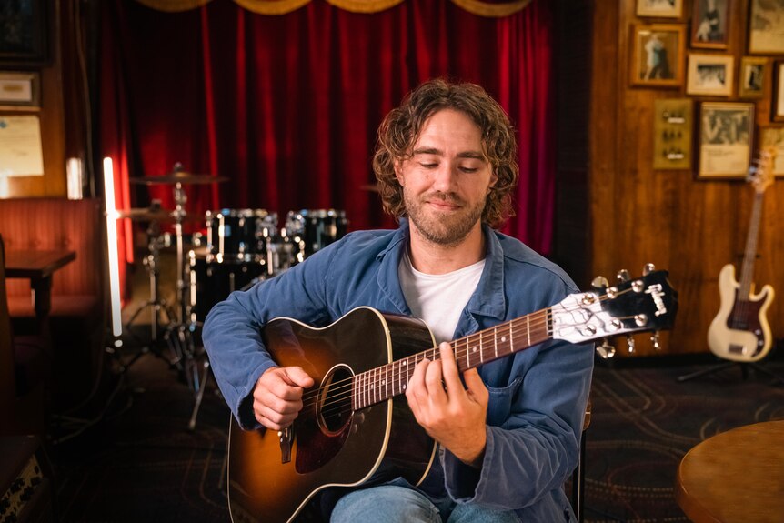 musician matt corby sits in a music room playing a guitar