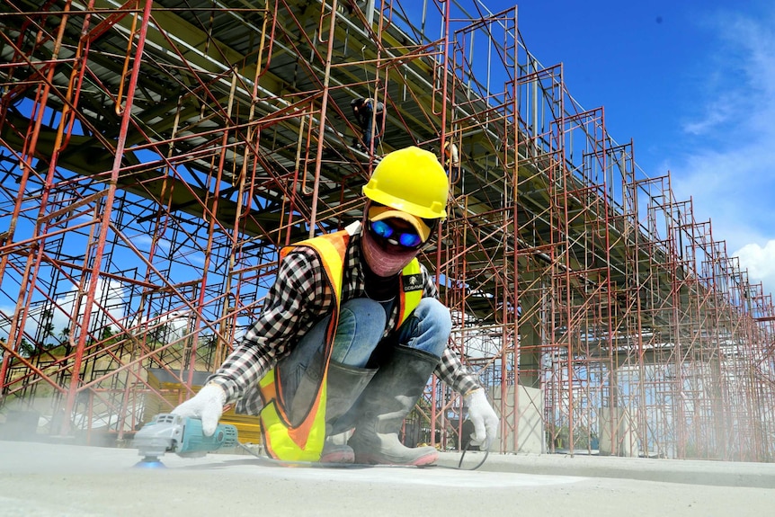 A construction worker crouched down buffering concrete in front of a huge half-built structure