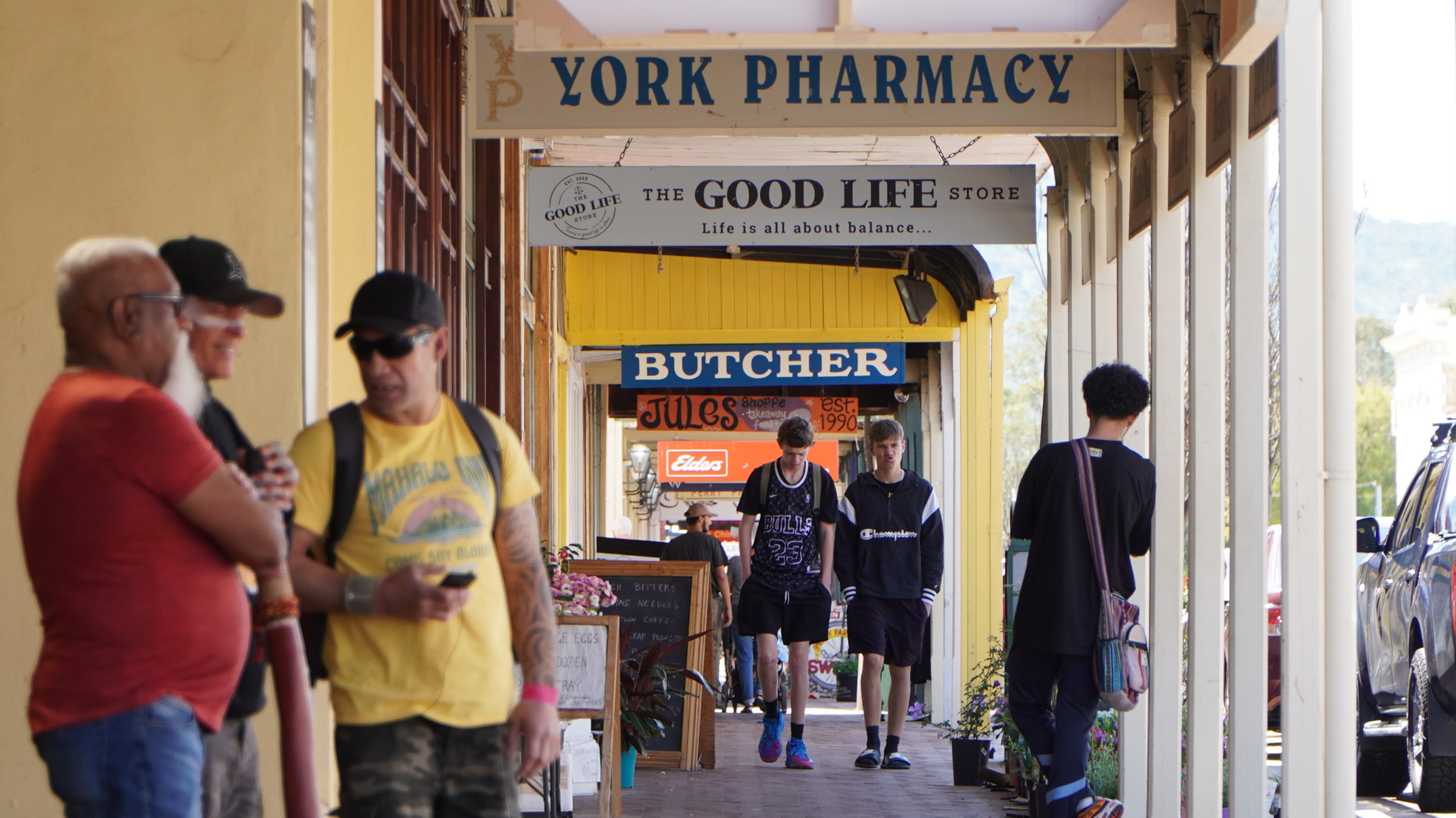 La gente camina por una acera cubierta en un camino rural lleno de tiendas.