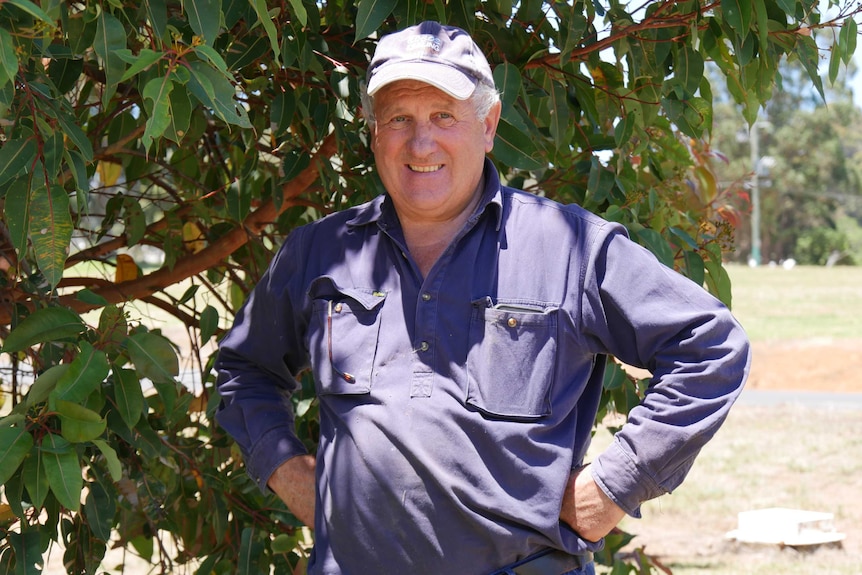 A man with a purple hat and shirt stands in front of trees.