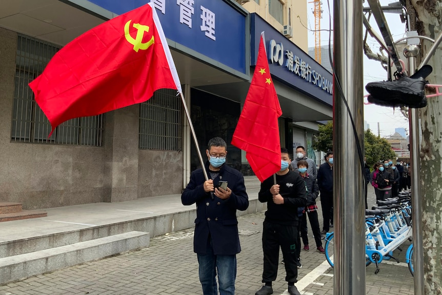 A man in mask carries the Communist Party flag. 