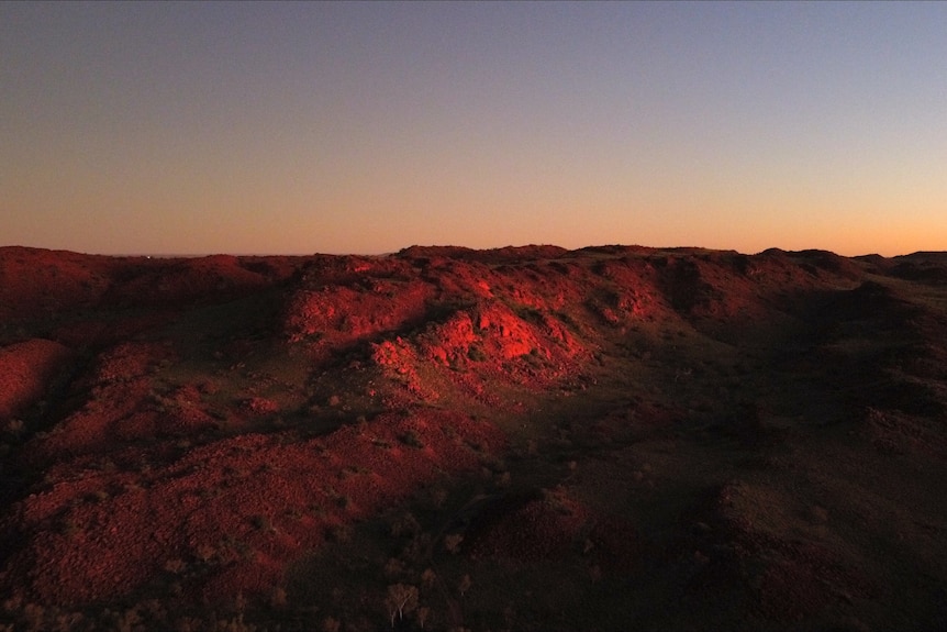 A wide landscape of red rock with the last dark blue and yellow light of the sun.