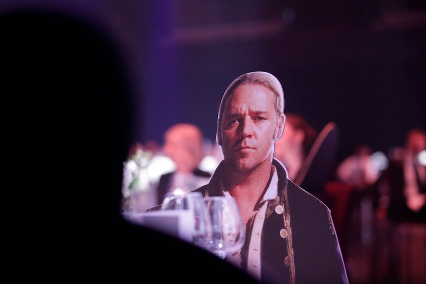 Cardboard cut-out of Russell Crowe in Master and Commander sitting at dining table in darkened room.