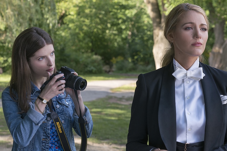 Colour still of Anna Kendrick holding camera and Blake Lively dressed in tux standing in park in 2018 film A Simple Favour.