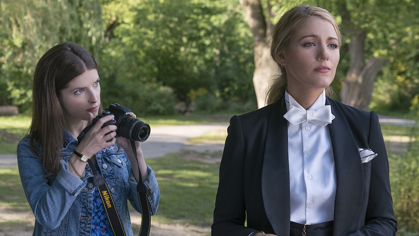 Colour still of Anna Kendrick holding camera and Blake Lively dressed in tux standing in park in 2018 film A Simple Favour.