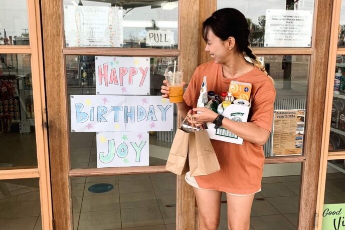 A young woman standing in front of the door into the road house with signs saying happy birthday joy. 