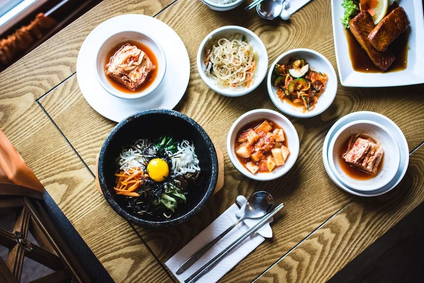 A photograph of a Korean meal served at a restaurant with kimchi, as well as other banchan, with a main meal of bibimbap
