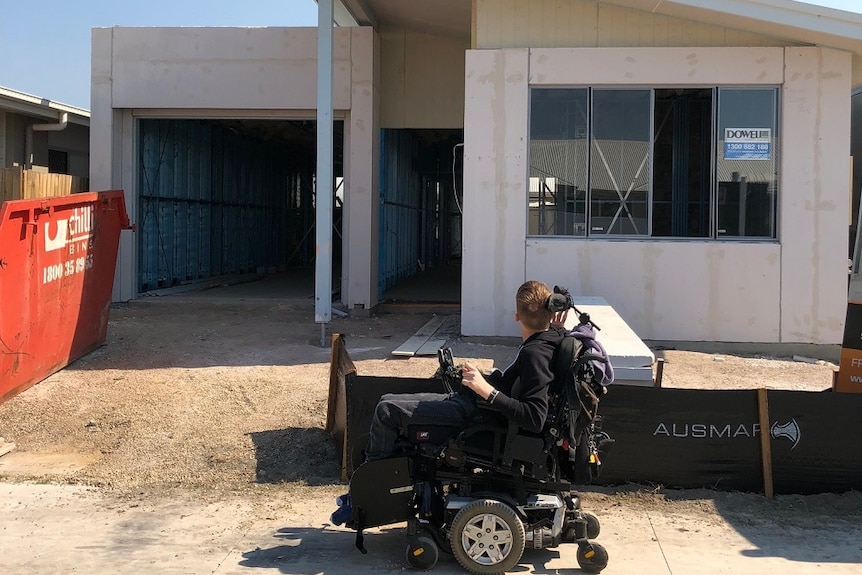 A man in a wheelchair outside a new house under construction