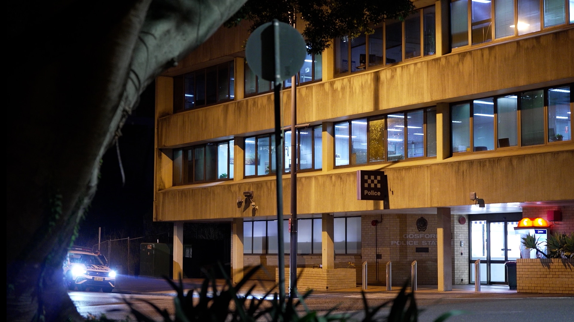 A concrete multi-story building with lights on inside and a Police sign at night.