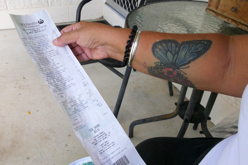 Se puede ver la mano sostiene el brazo del recibo de compras con un tatuaje de mariposa