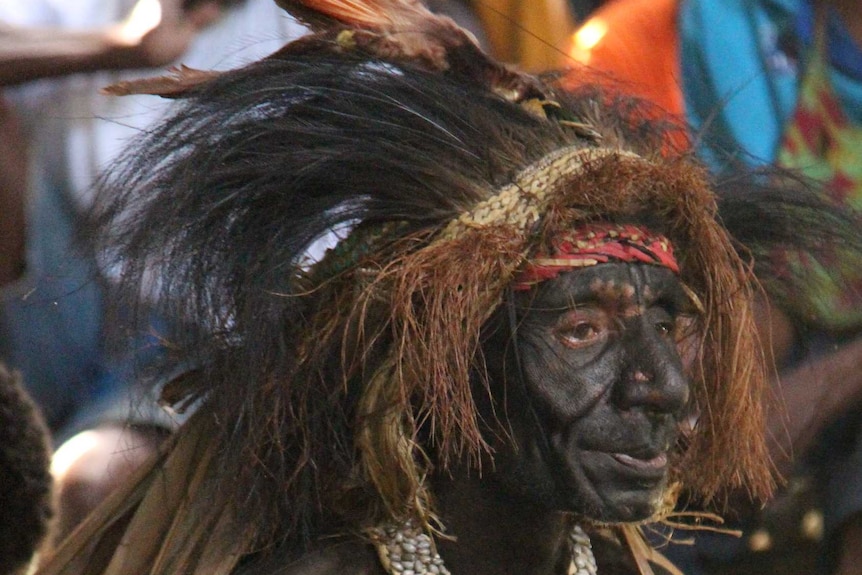 A man wearing tribal dress sits cross-legged holding a photograph.