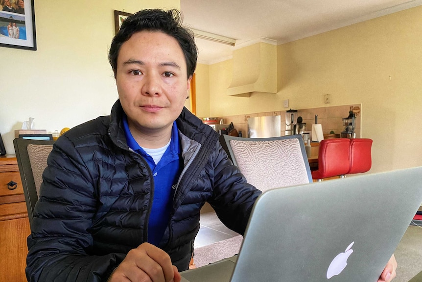 A man sitting at a table behind a laptop