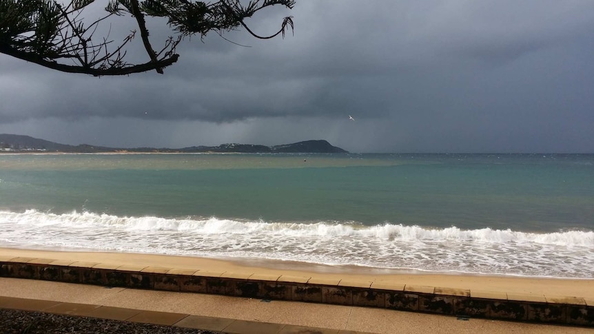 A stormy sky over a beach, with a dark ocean, discoloured section of water and a dark coastline.