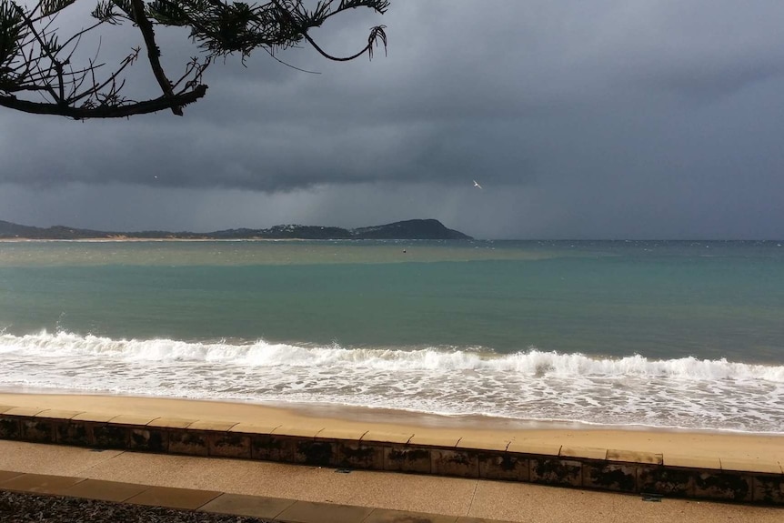 A stormy sky over a beach, with a dark ocean, discoloured section of water and a dark coastline.