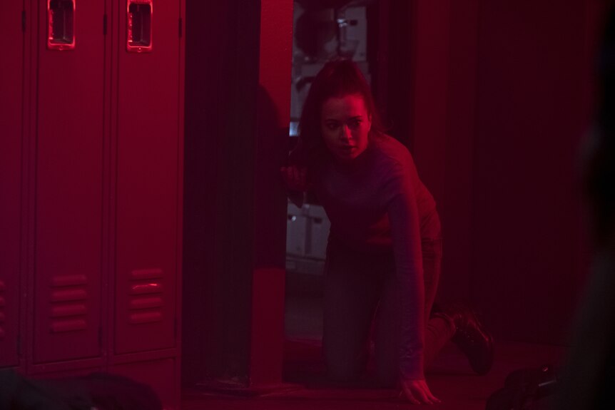 A young woman crouching on her knees in a room bathed in red light