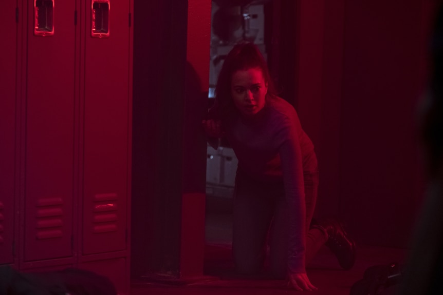 A young woman crouching on her knees in a room bathed in red light