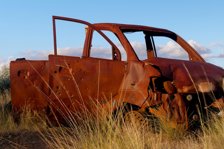 A completely rusted car body is lit from behind by blue sky