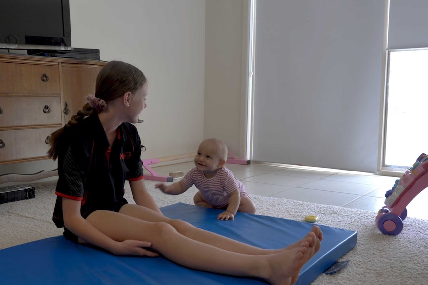 A young girl and her baby sister sitting on their living room floor and laughing together