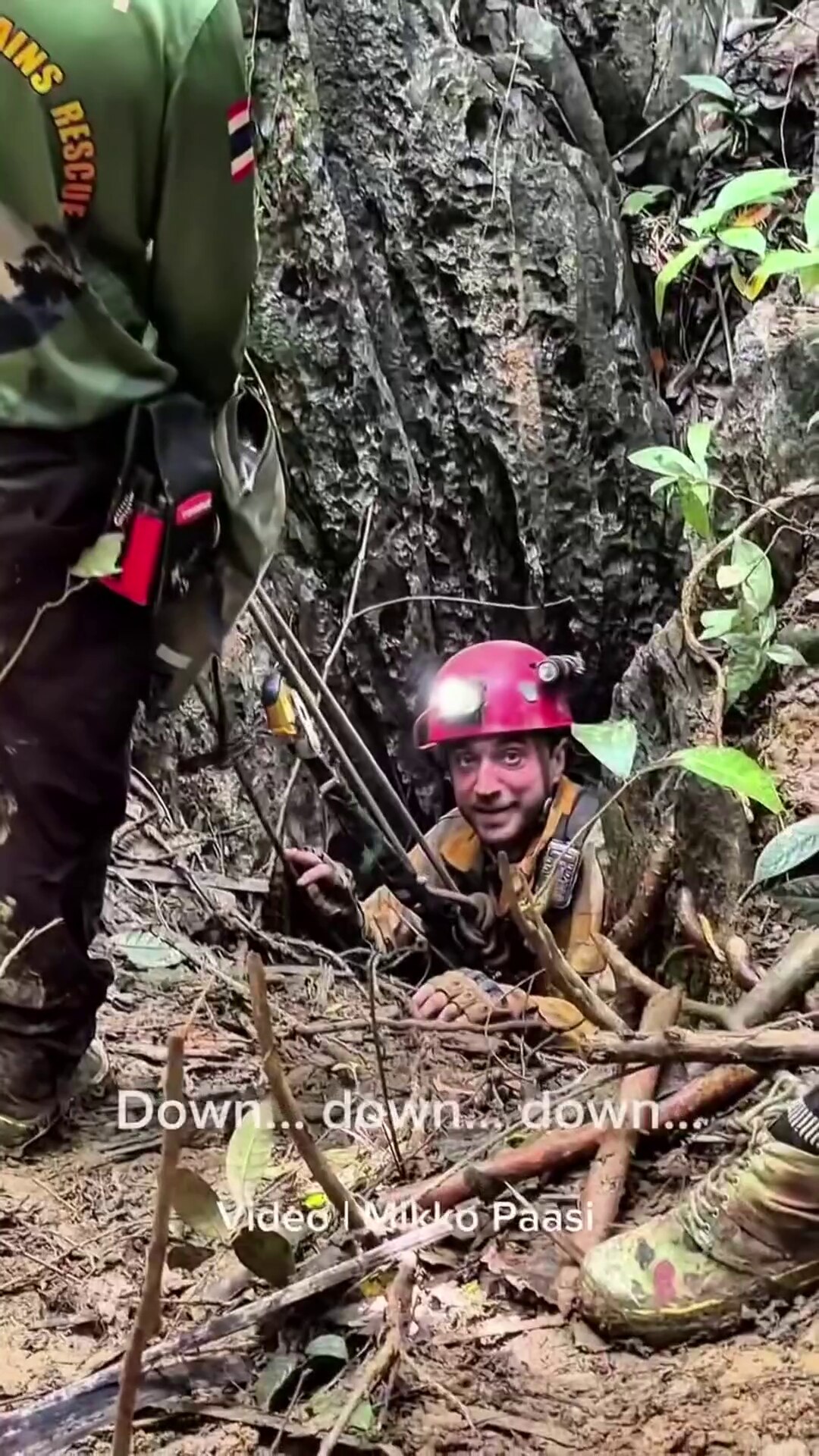 Cave diver wearing protective gear prepares to descend into narrow opening.