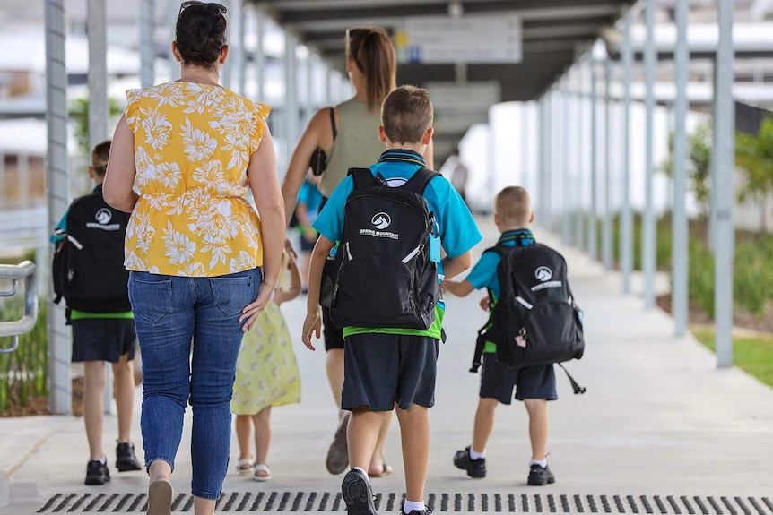 Parent walks children in school uniform into Spring Mountain State School, west of Brisbane.