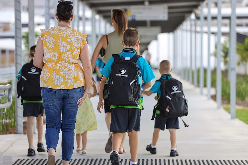 Parent walks children in school uniform into Spring Mountain State School, west of Brisbane.