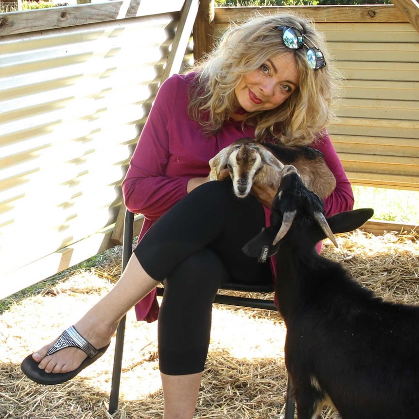 ABC presenter Sheridan Stewart sits on a chair with a baby goat on her lap.