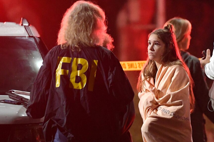 A young woman speaks to an FBI officer with red police lights flashing in the background after a mass shooting in California.