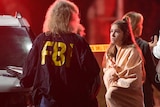 A young woman speaks to an FBI officer with red police lights flashing in the background after a mass shooting in California.