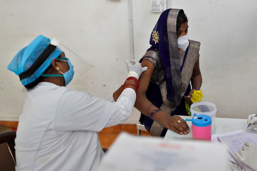 A nurse in protective gear injects a woman with a vaccine inside a clinic.